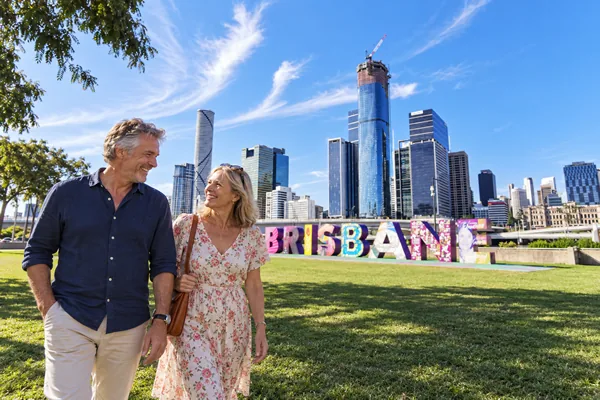 Couple walking past the Brisbane sign with the city skyline behind