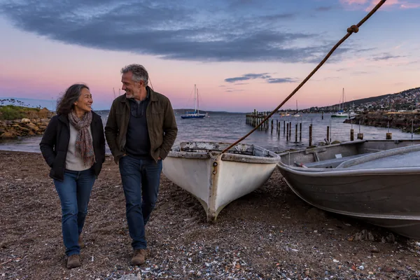 Couple strolling past boats on the shore near Battery Point, Hobart, at dusk