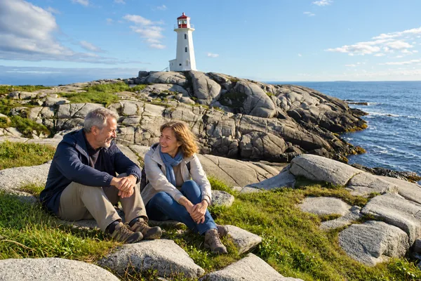 Couple sitting on the granite rocks below Peggys Cove lighthouse, Nova Scotia