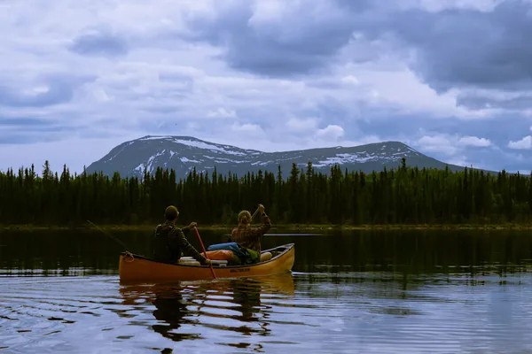 Two people paddling a canoe across a calm northern lake below the mountains