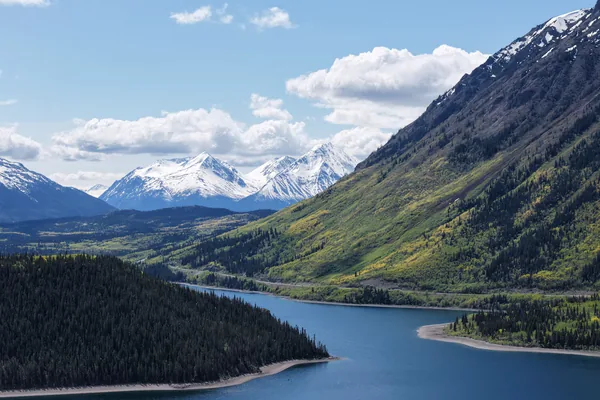 Snow capped mountains above a lake and forest in Yukon