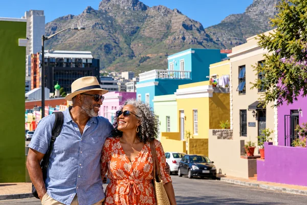 Couple walking arm in arm past colourful houses in Cape Town with the mountain behind